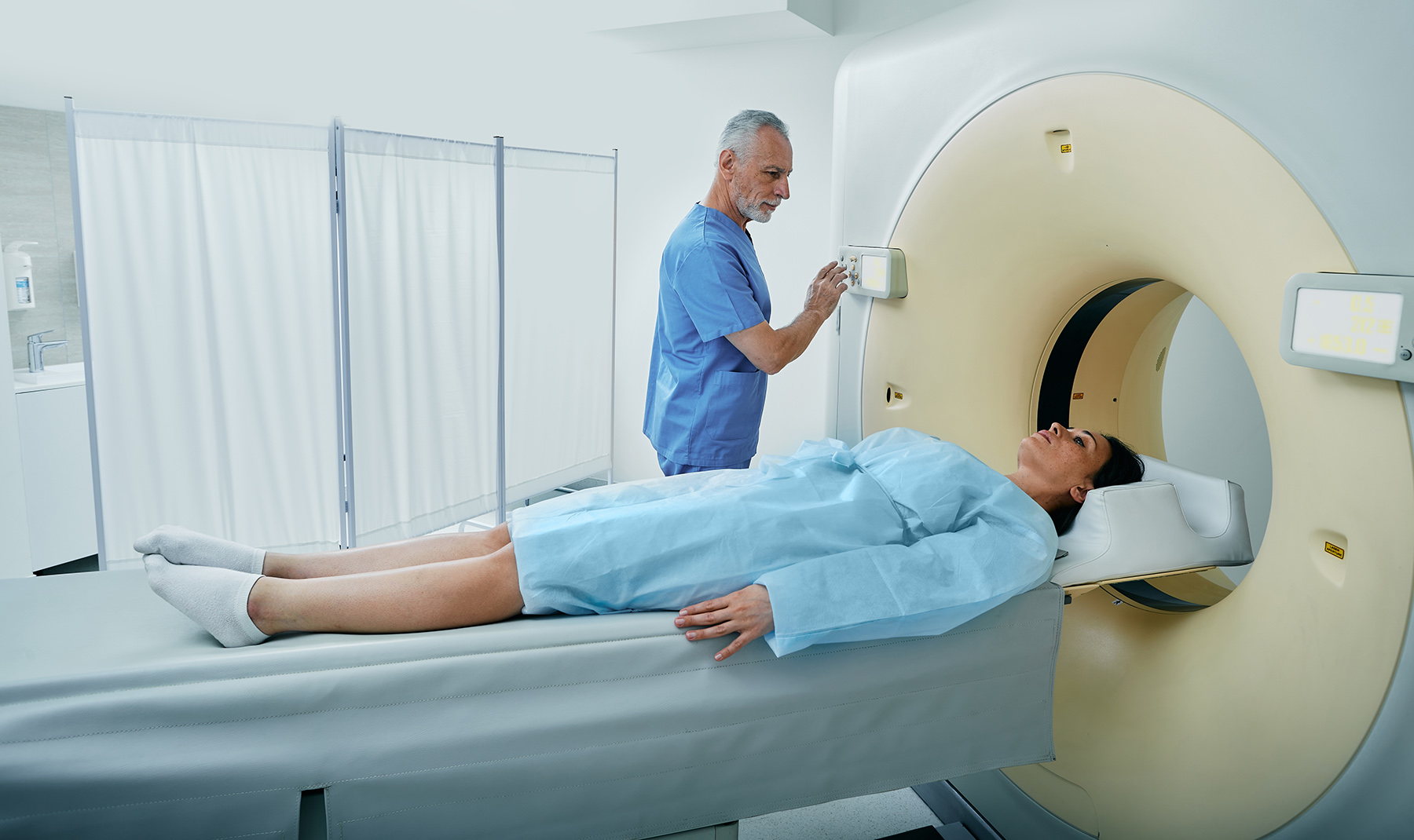 CT scan technologist overlooking woman patient in CT scanner during settings on Computed Tomography scanner